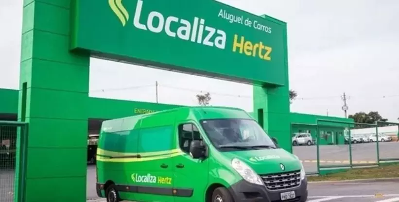 A foto mostra uma van da empresa Localiza saindo da agência