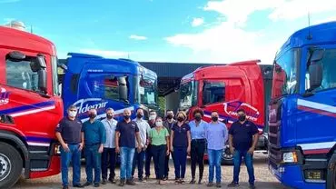 A foto mostra 4 caminhões da Ademir Transportes e vários motoristas