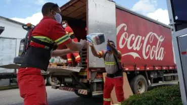 A foto mostra três ajudantes descarregando um caminhão da Coca-Cola