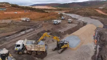 A foto mostra uma escavadeira hidráulica e vários caminhões basculantes da Construtora Terraço em uma operação de mineração